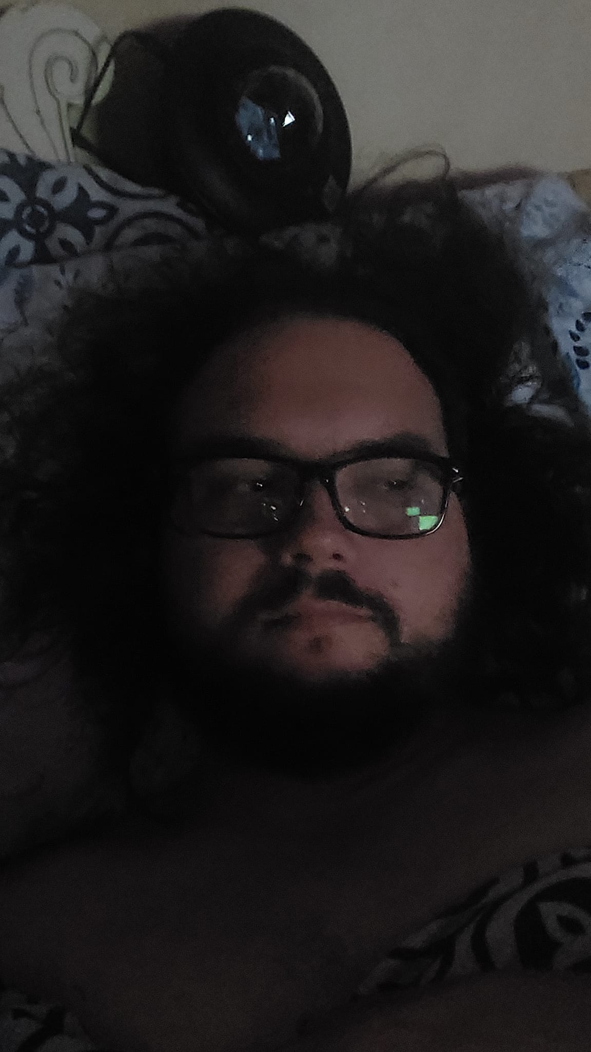 A man with long dark hair and a beard is in bed, the lighting is bad, photo 2